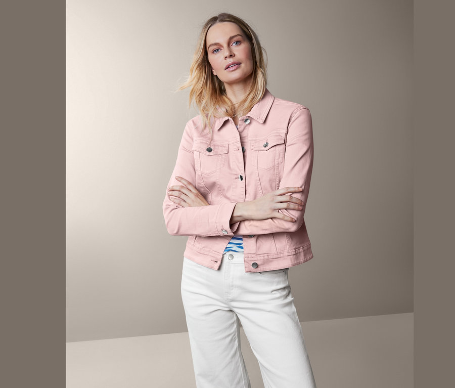 Nő pózol rózsaszín farmerdzsekiben és fehér nadrágban.