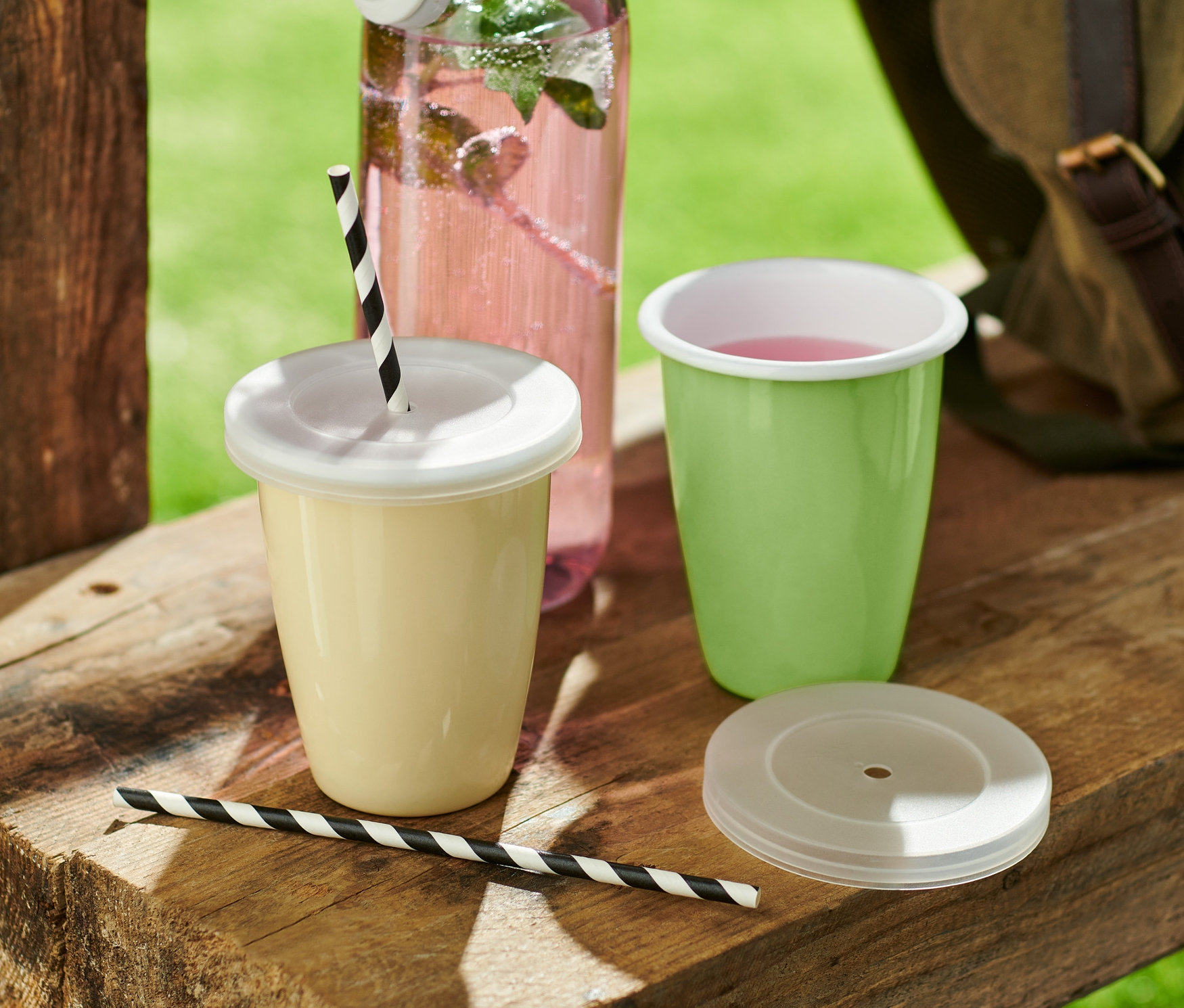 Két piknikbögre és egy üveg ital egy fa asztalon.