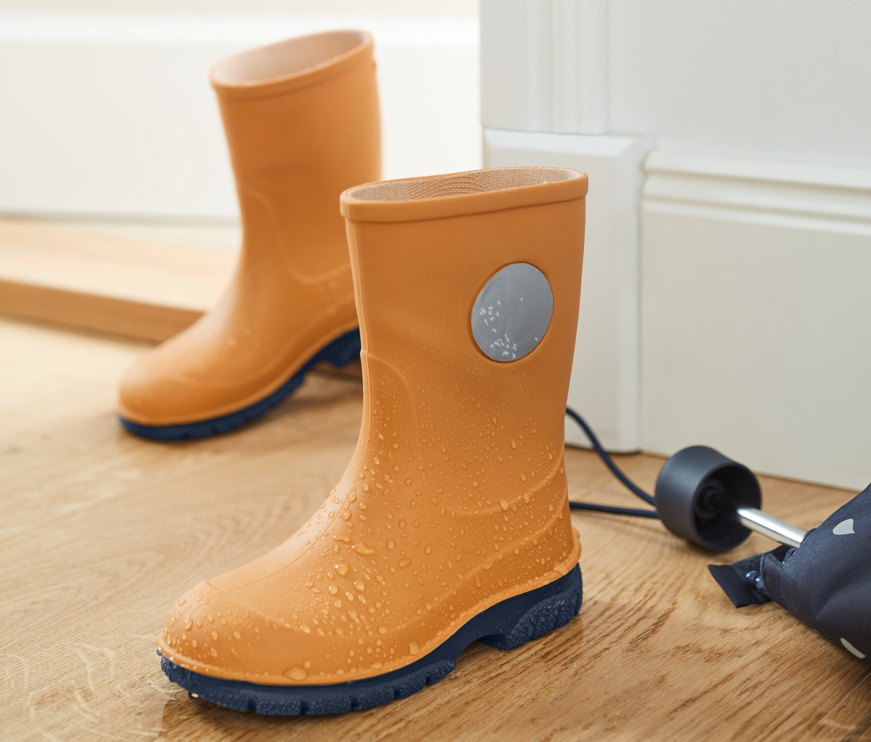 Két pár gumicsizma áll egy fapadlón egy esernyő mellett.