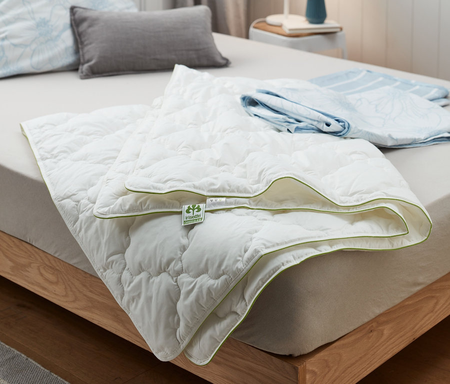 Az ágyon egy fehér irisette® greenline steppelt nyári paplan fekszik világoszöld szegéllyel.