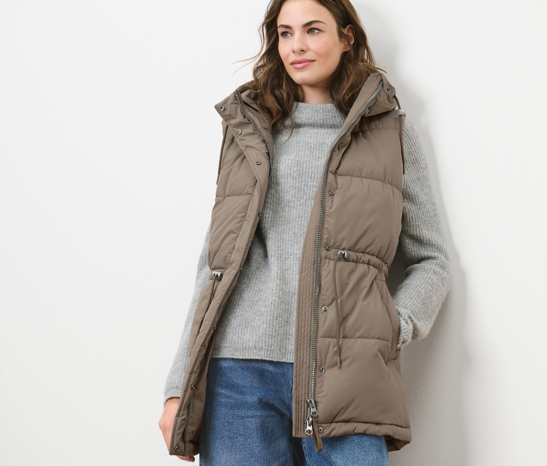 Nő visel steppelt mellényt, pulóvert és farmert.