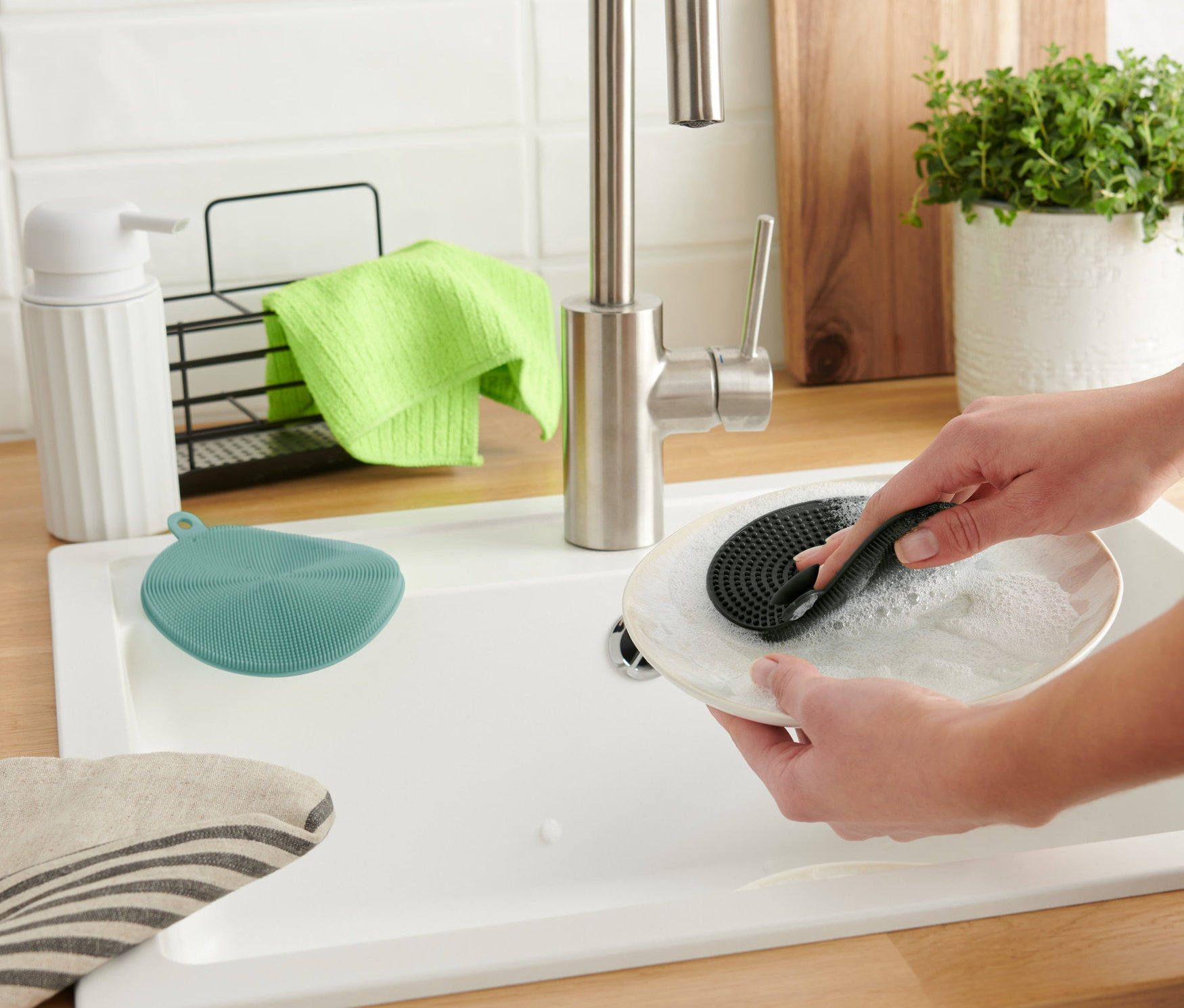 Egy nő tányért mos 2 szilikon mosogatószivaccsal.