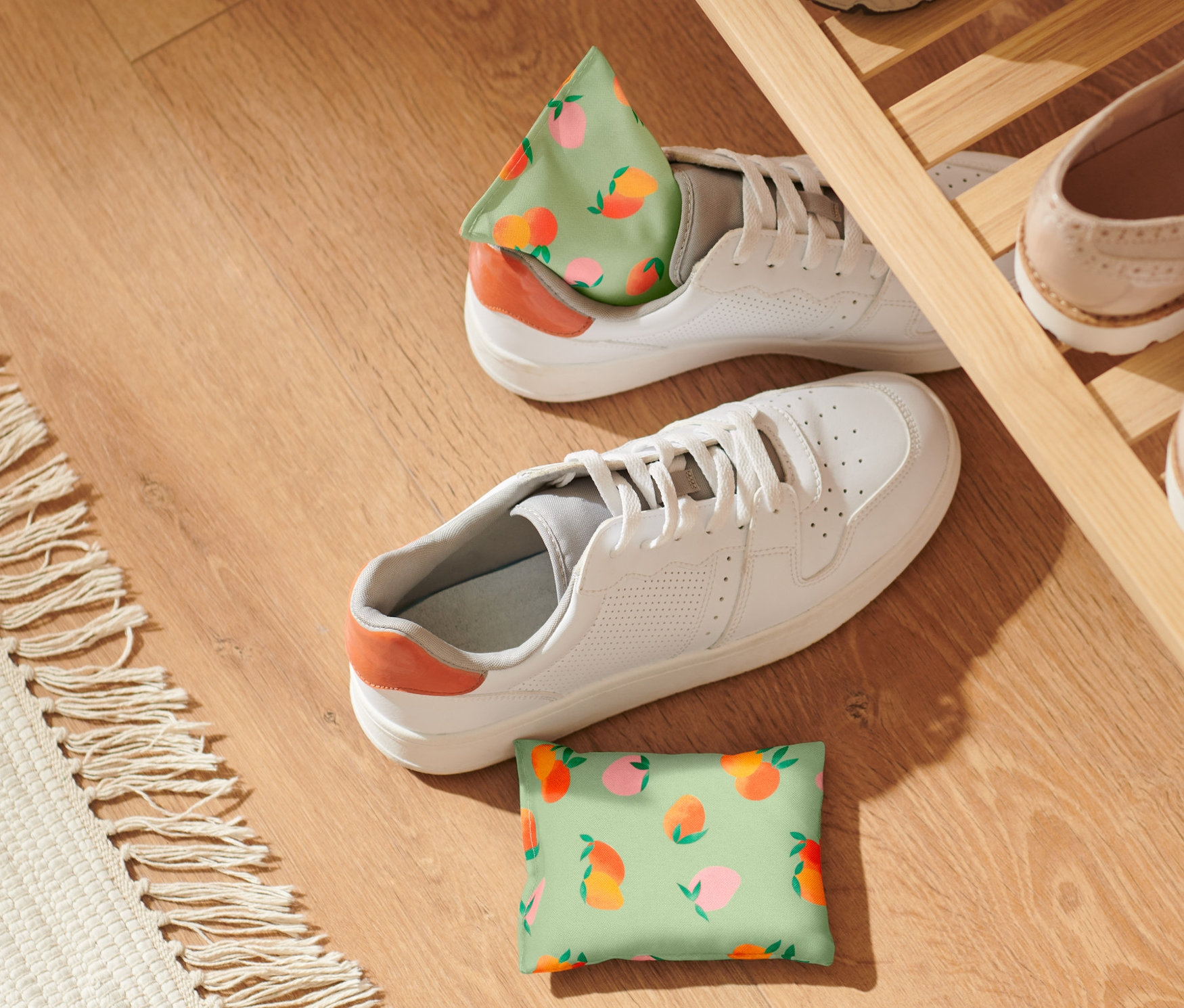 Két barackmintás frissítő párnácska fekszik fehér cipők mellett egy fapadlón.