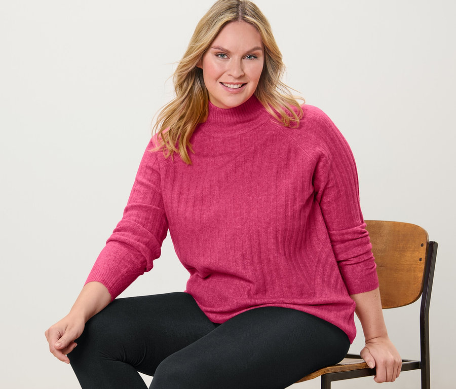 Nő ül egy széken, és kötött pulóvert és termoleggingset visel.