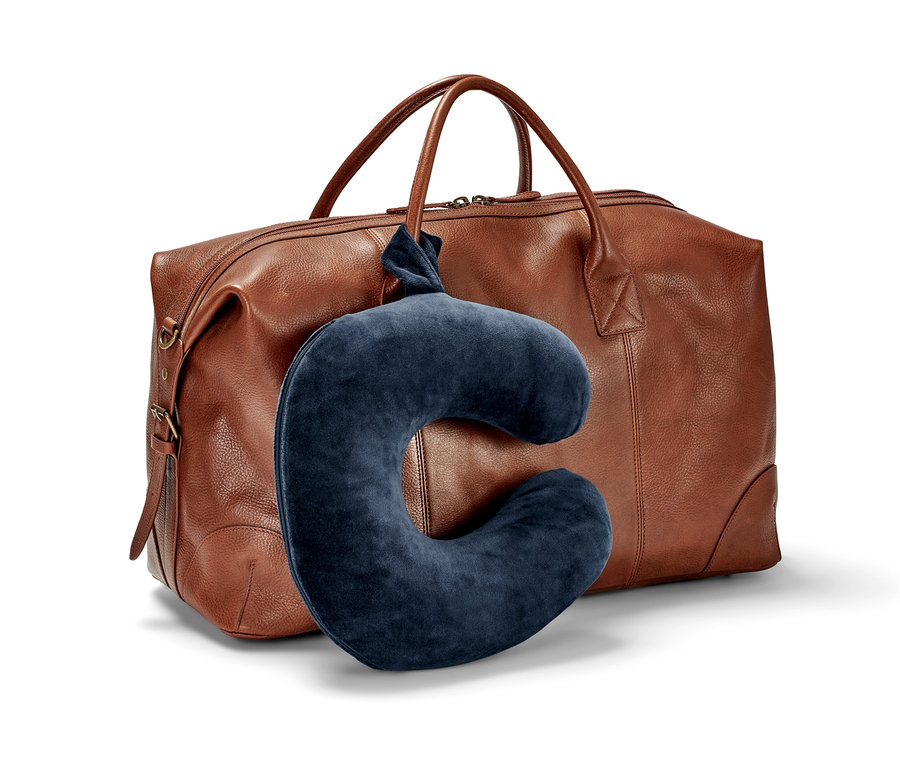 Egy sötétkék memóriahabos nyakpárna egy barna bőr utazótáskának van támasztva.