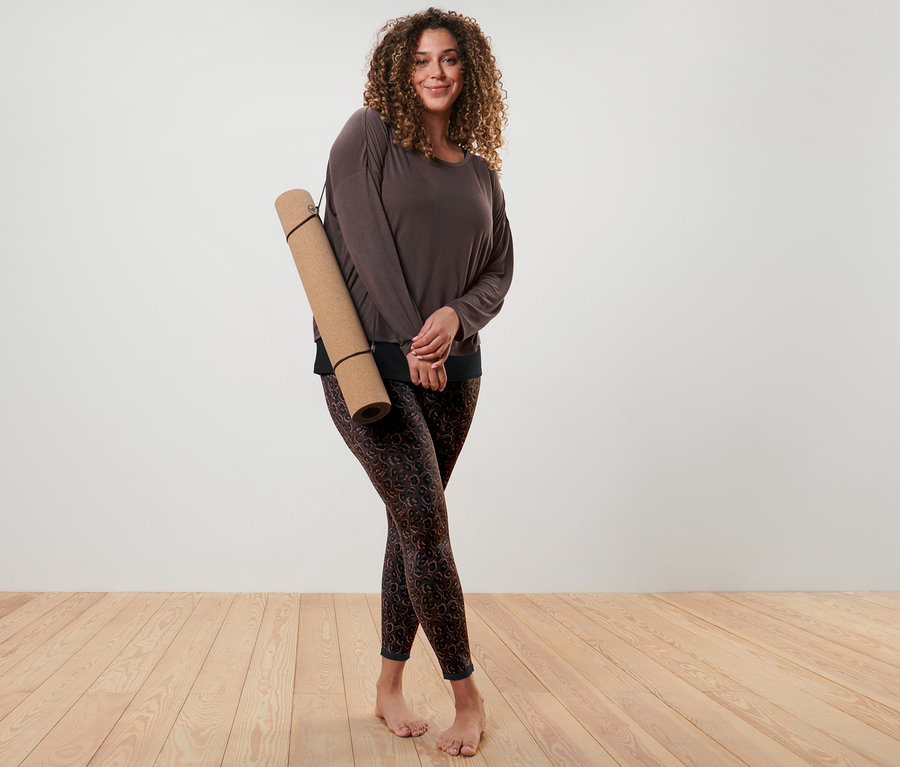 Nő pózol barna 2 az 1-ben sportfelsőben és fekete-barna kifordítható sportnadrágban.