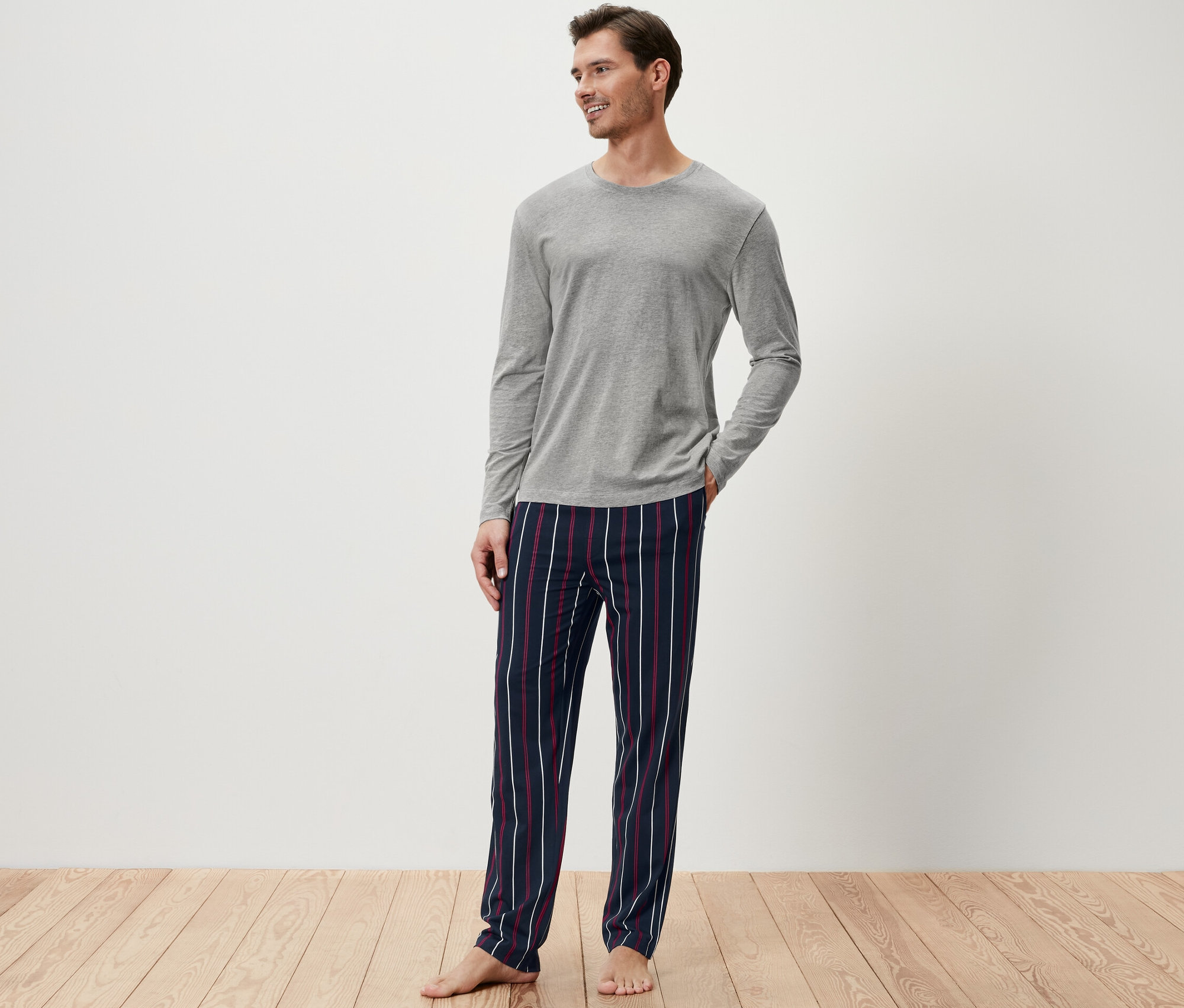 Férfi szürke pizsama felsőben és csíkos pizsama alsóban.