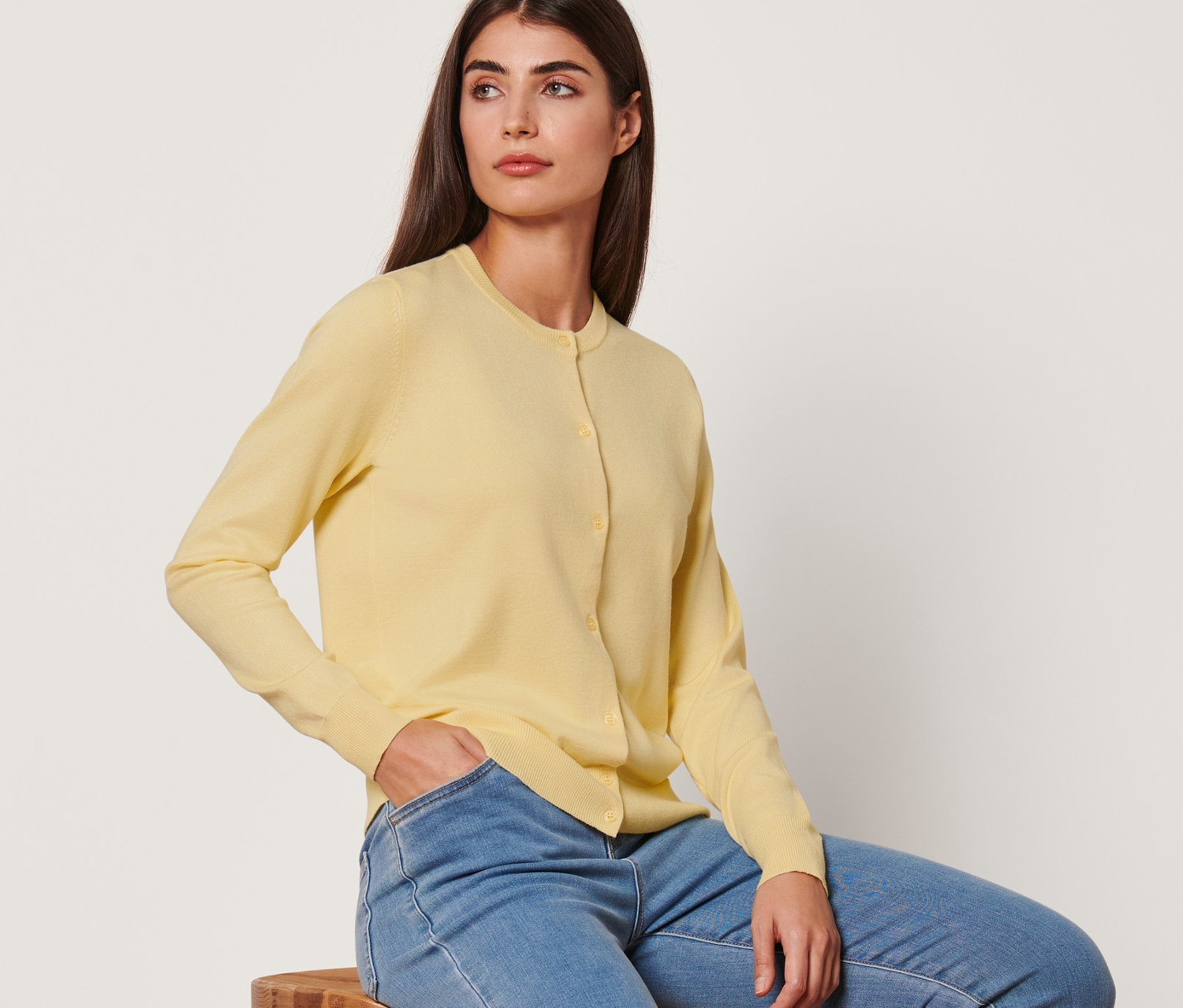 Egy nő egy széken ül, és sárga, finomkötésű kardigánt és farmert visel.