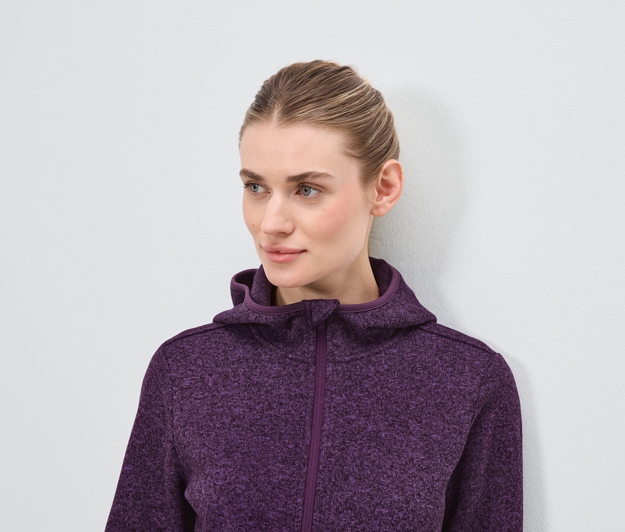 Portré egy szőke hajú nőről lila kapucnis pulóverben.