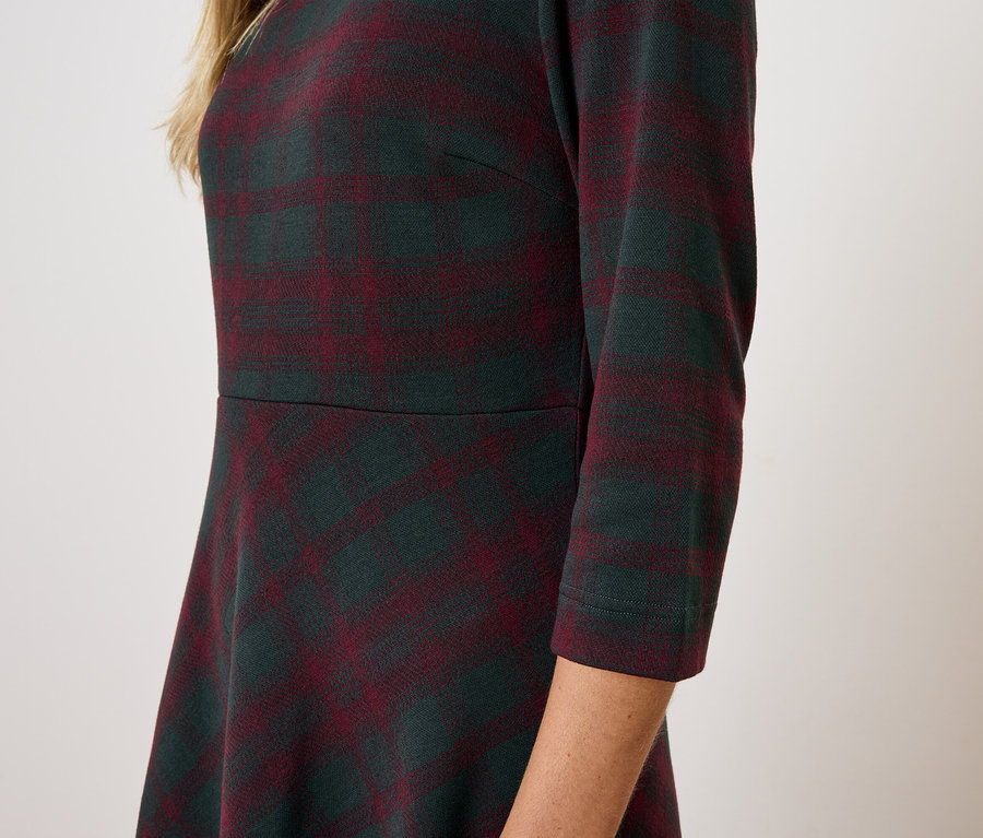 Oldalnézet egy nőről, aki háromnegyedes ujjú kockás ruhát visel.