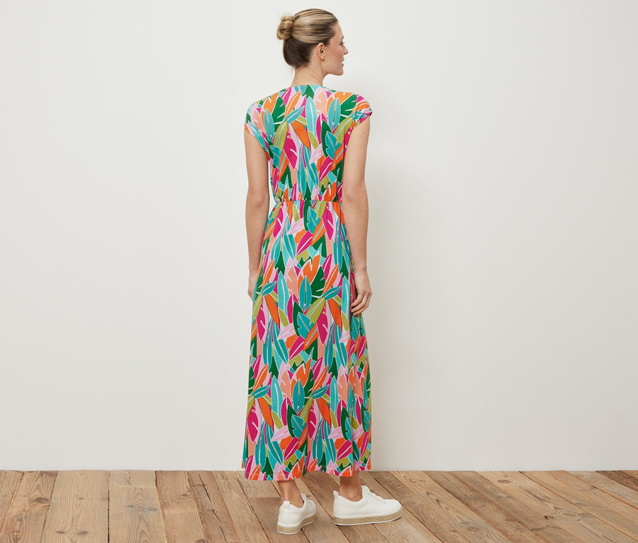 Egy nő háttal áll a kamerának, jersey ruhát visel csomókkal és fehér tornacipőt.