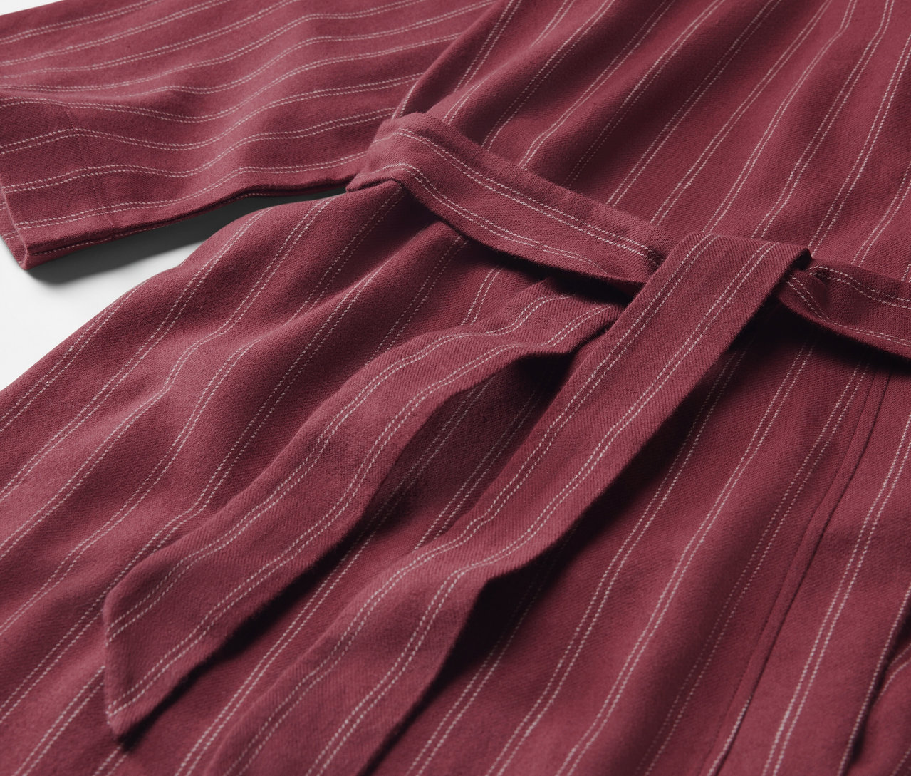 Egy bordó, csíkos köntös részlete, megkötött övvel.