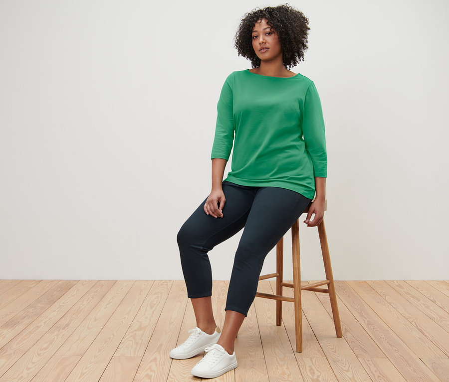 Nő ül egy széken, zöld, 3/4-es ujjú felsőt visel.