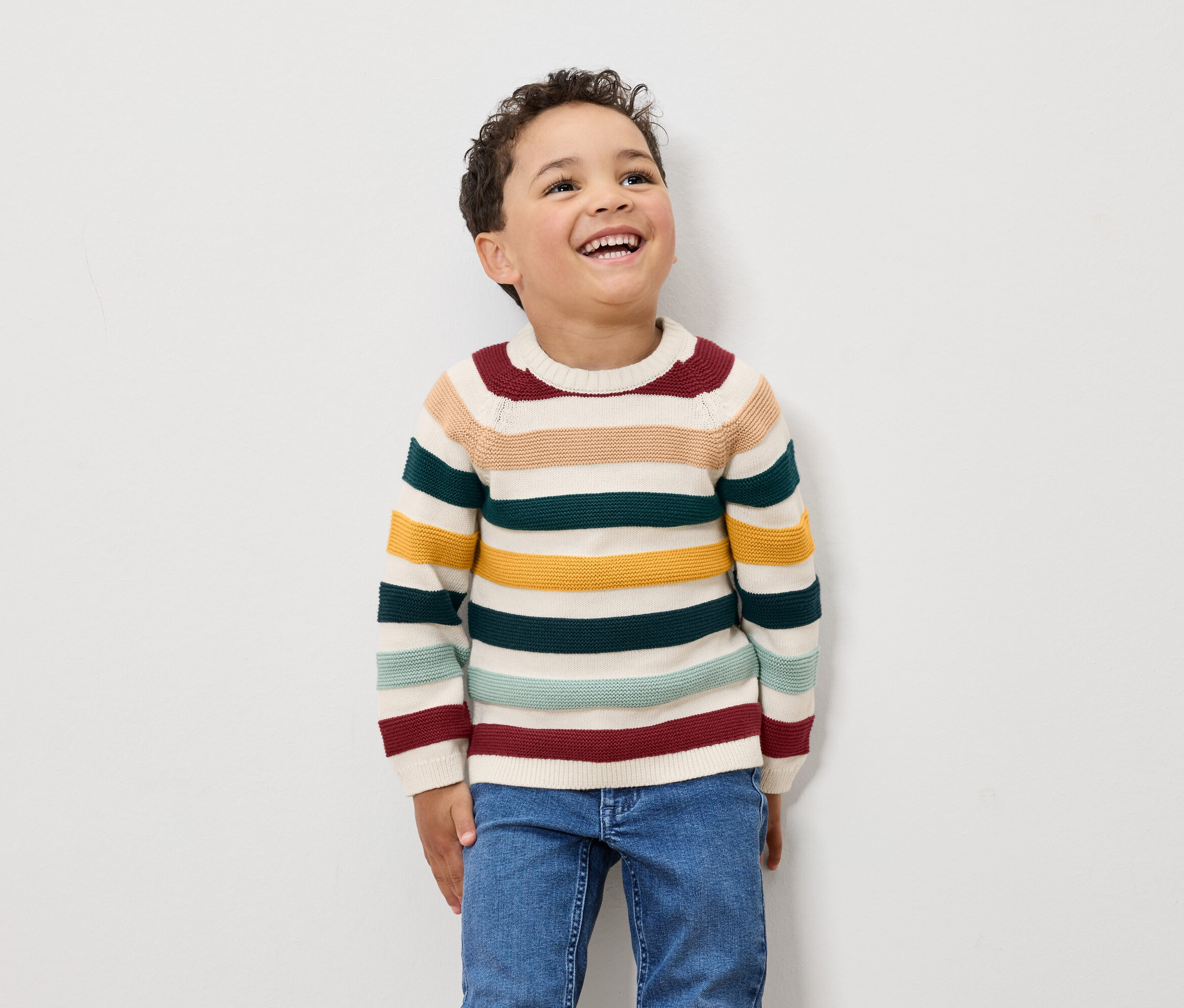 Egy fiú nevet, csíkos pulóvert és farmert visel.