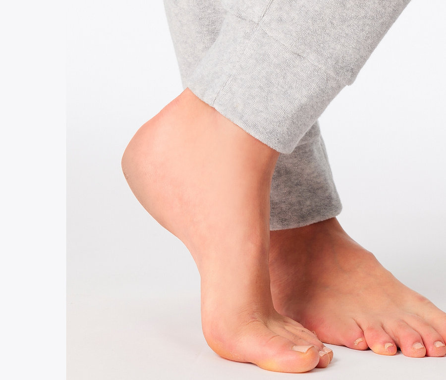 Egy fehér háttéren álló, szürke melegítőnadrágot viselő személy lábai.