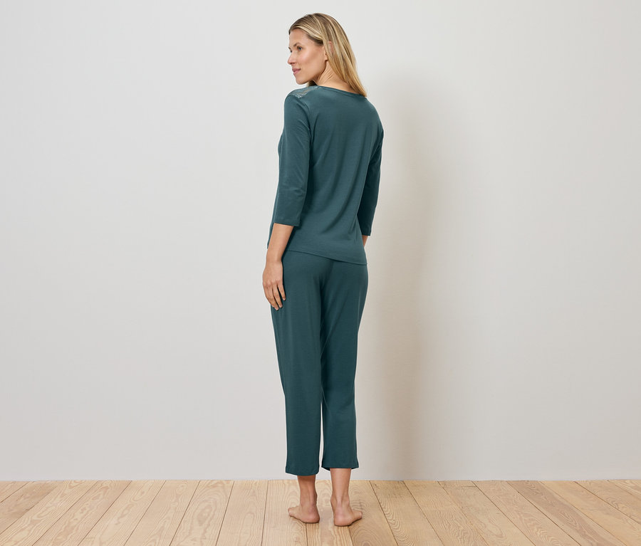 Nő zöld pizsamában áll a fapadlón.