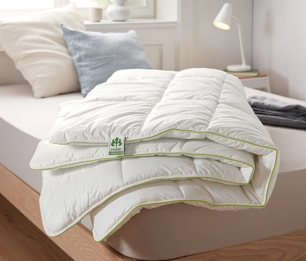 Egy összehajtott irisette® greenline termopaplan fehér felülettel és zöld szegéllyel fekszik egy ágyon.
