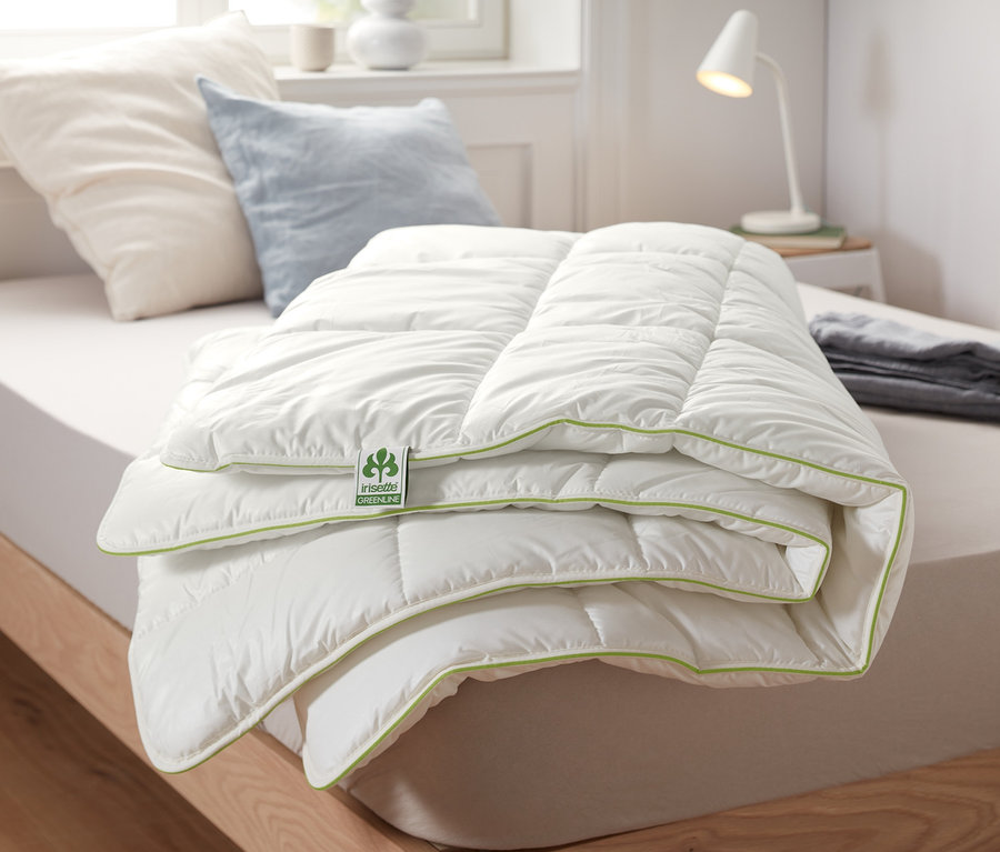 Egy összehajtott irisette® greenline termopaplan fehér felülettel és zöld szegéllyel fekszik egy ágyon.