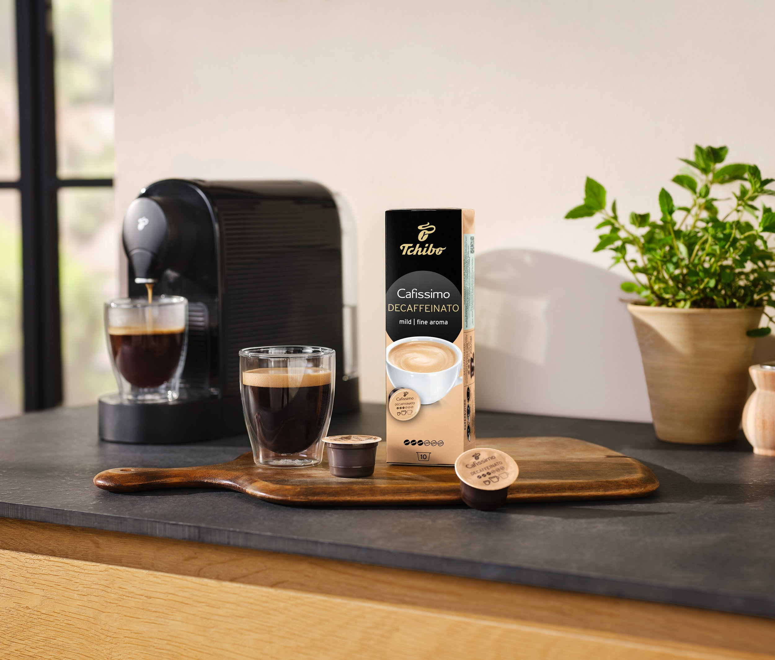 Kávéfőző kávét önt egy pohárba egy csomag Cafissimo Decaffeinato kapszula mellett.