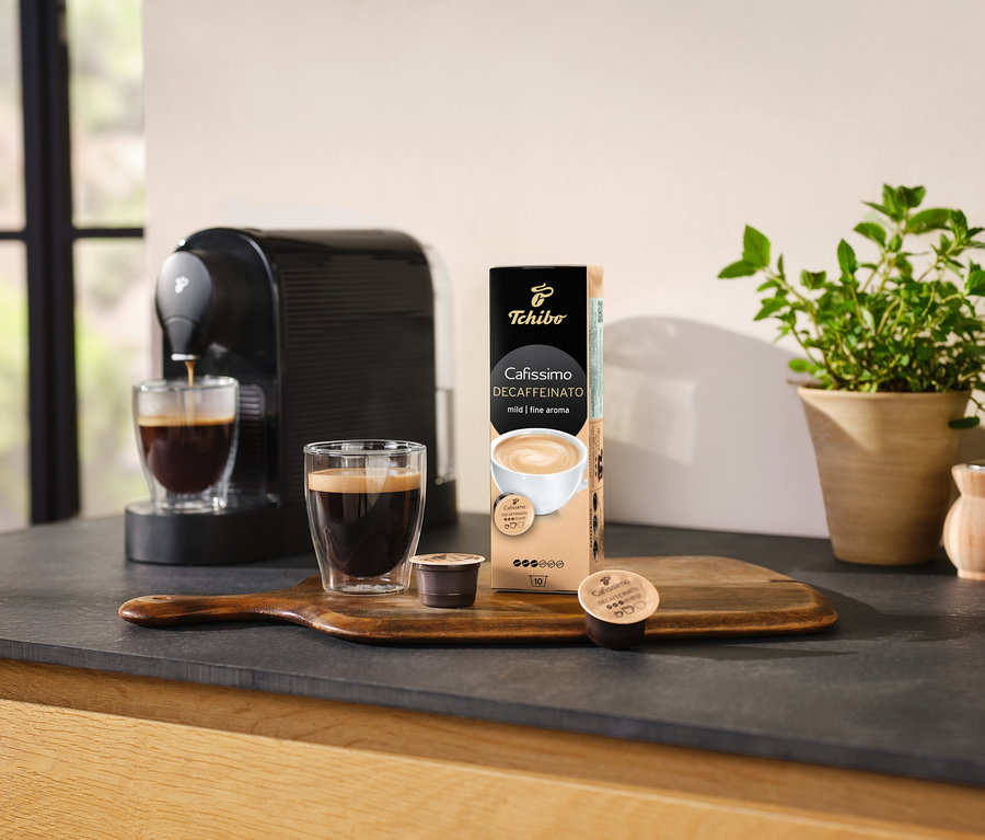 Kávéfőző kávét önt egy pohárba egy csomag Cafissimo Decaffeinato kapszula mellett.