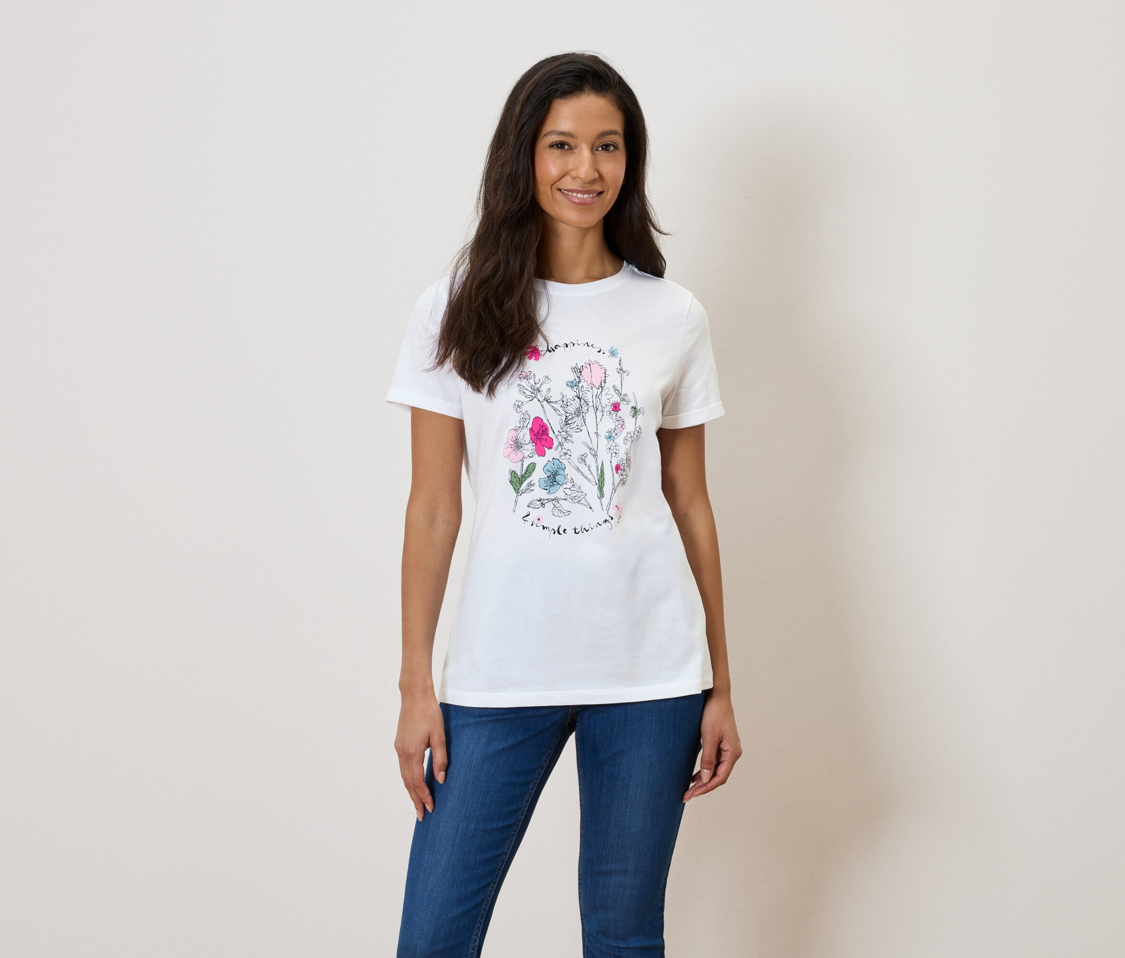 Nő virágmintás fehér pólót és kék farmert visel.