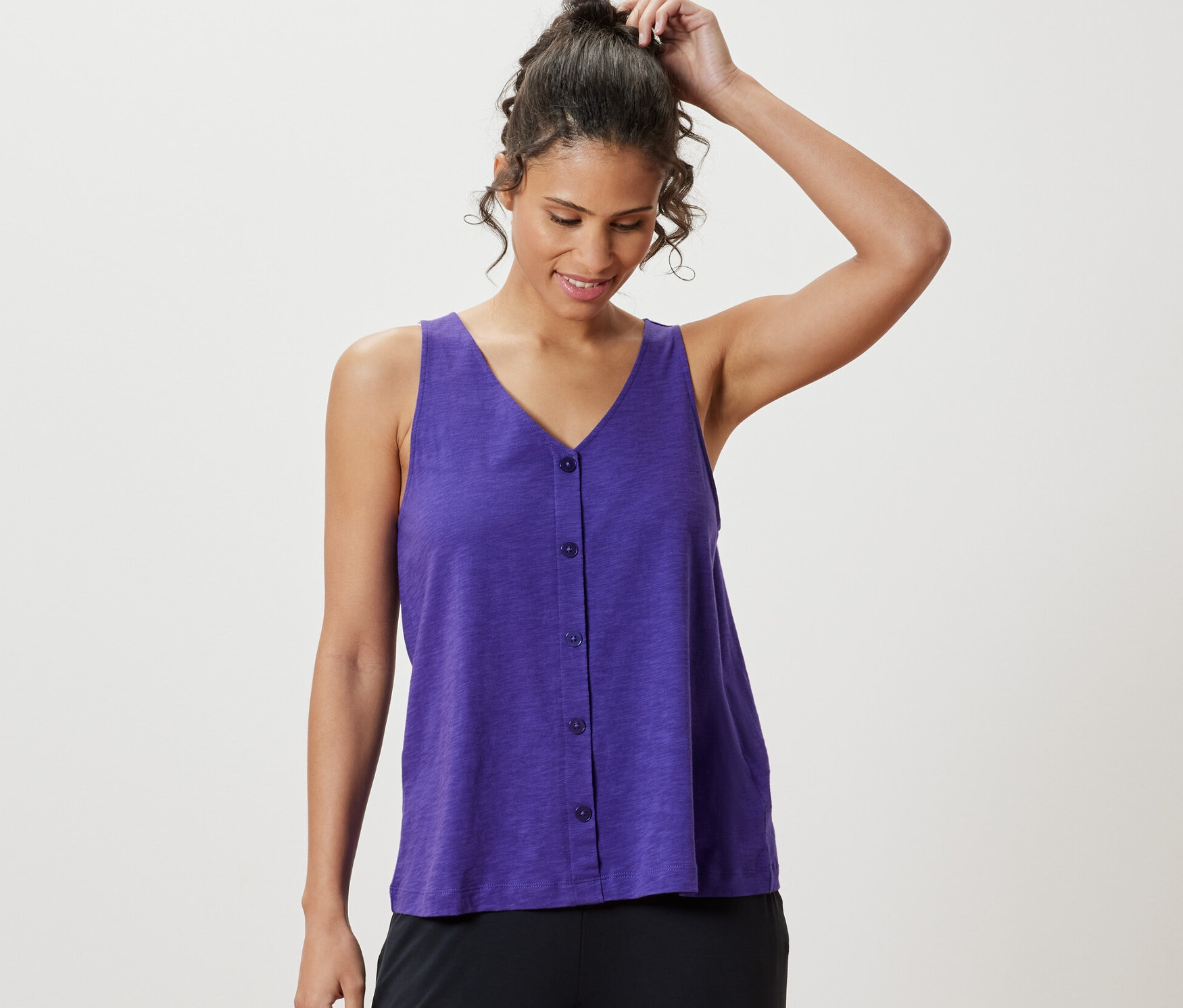 Nő igazítja a haját, lila, modálkeverékből készült topot visel.