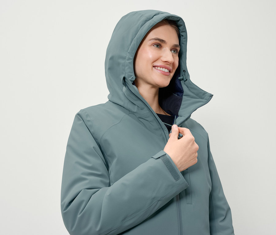 Nő zárja a kékeszöld, kapucnis kabátot.