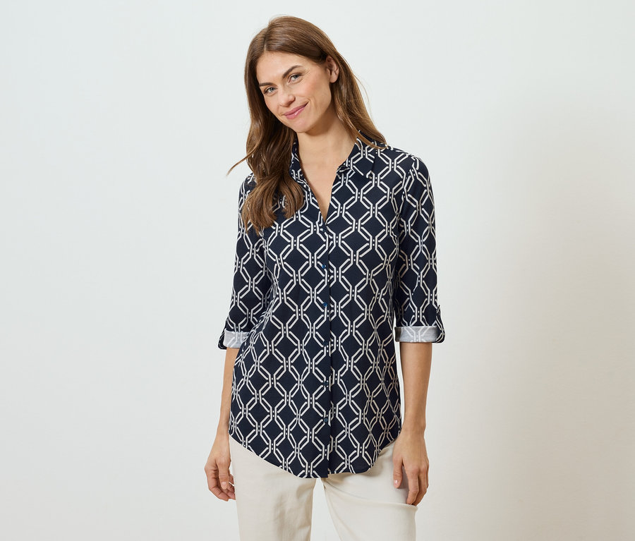 Nő visel egy fehér geometrikus mintás tengerészkék blúzt és bézs nadrágot.