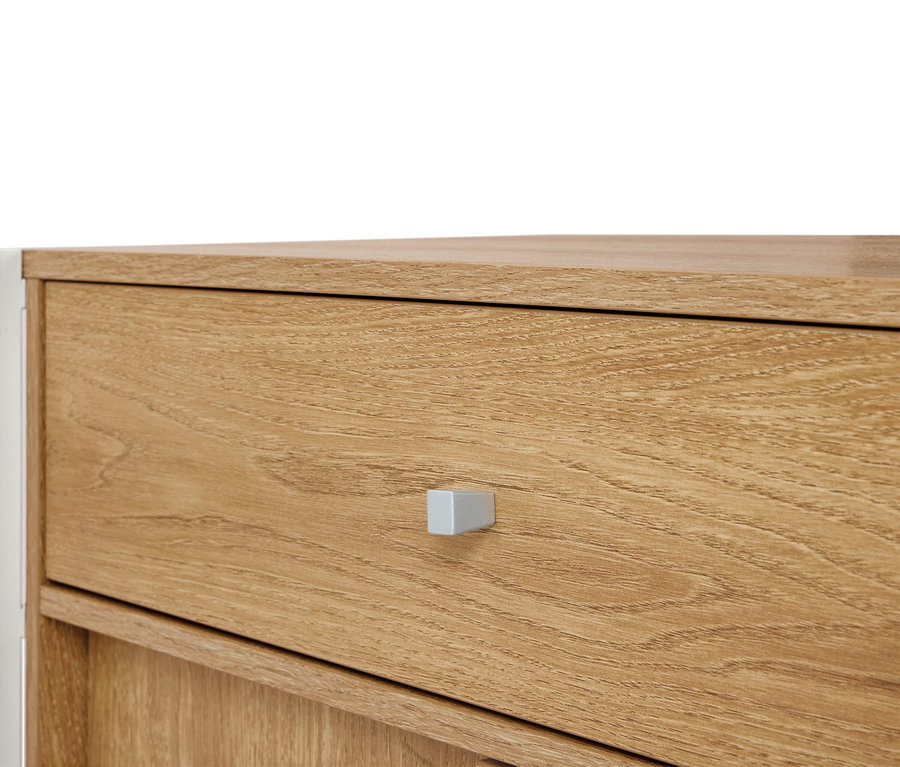 Egy világosbarna fa komód közeli képe ezüst fogantyúval.
