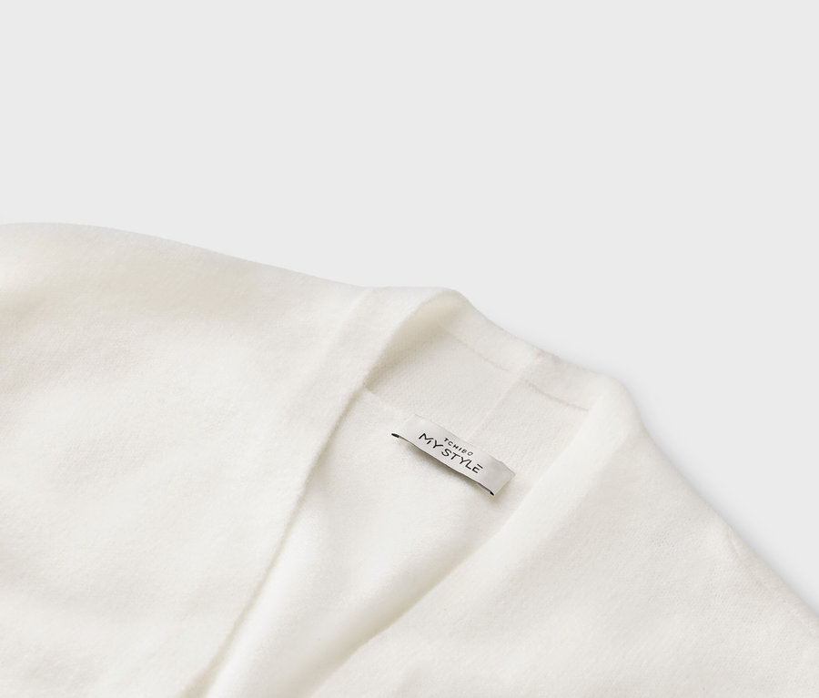 Egy fehér kötött kardigán közelképe, rajta egy „TCHIBO MY STYLE” feliratú címke.