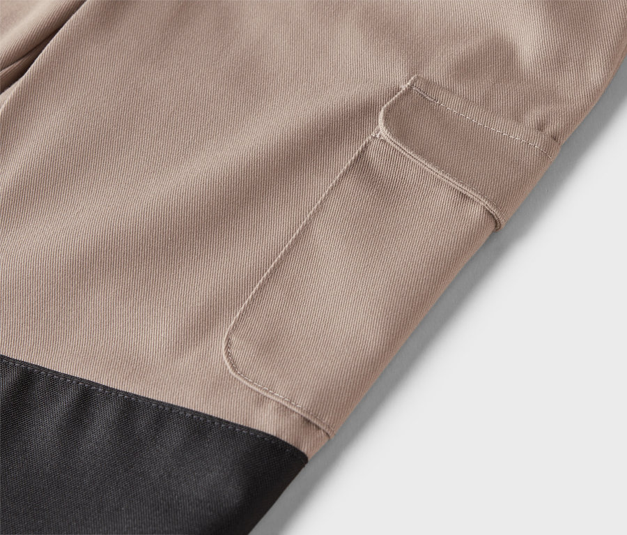 Egy bézs színű nadrág közeli képe, rávarrt zsebbel és fekete alsó résszel.