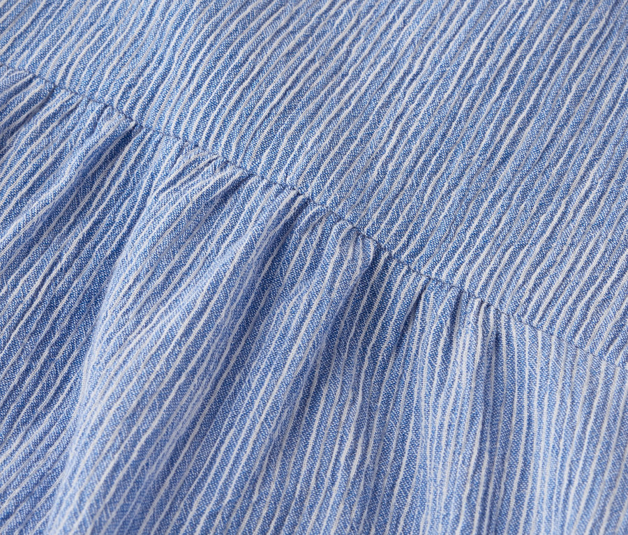Kék-fehér csíkos szövet ráncolt részleteinek közeli képe.