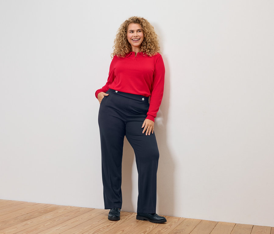 Göndör hajú nő piros felsőben és kék nadrágban.