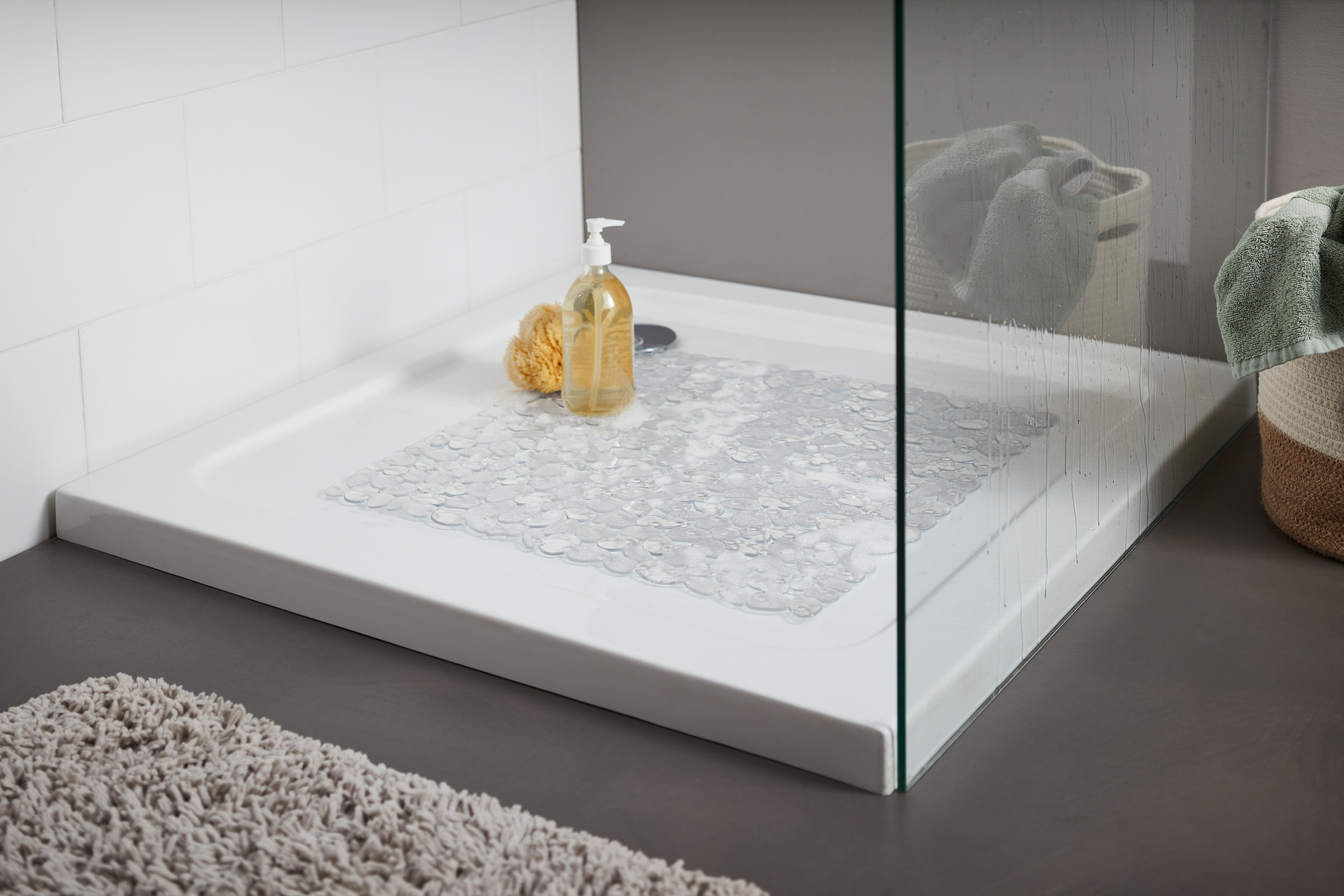 Zuhanytálca átlátszó zuhanytálcabetéttel. A tálcán egy sárga fürdőszivacs és egy pumpás üveg található.