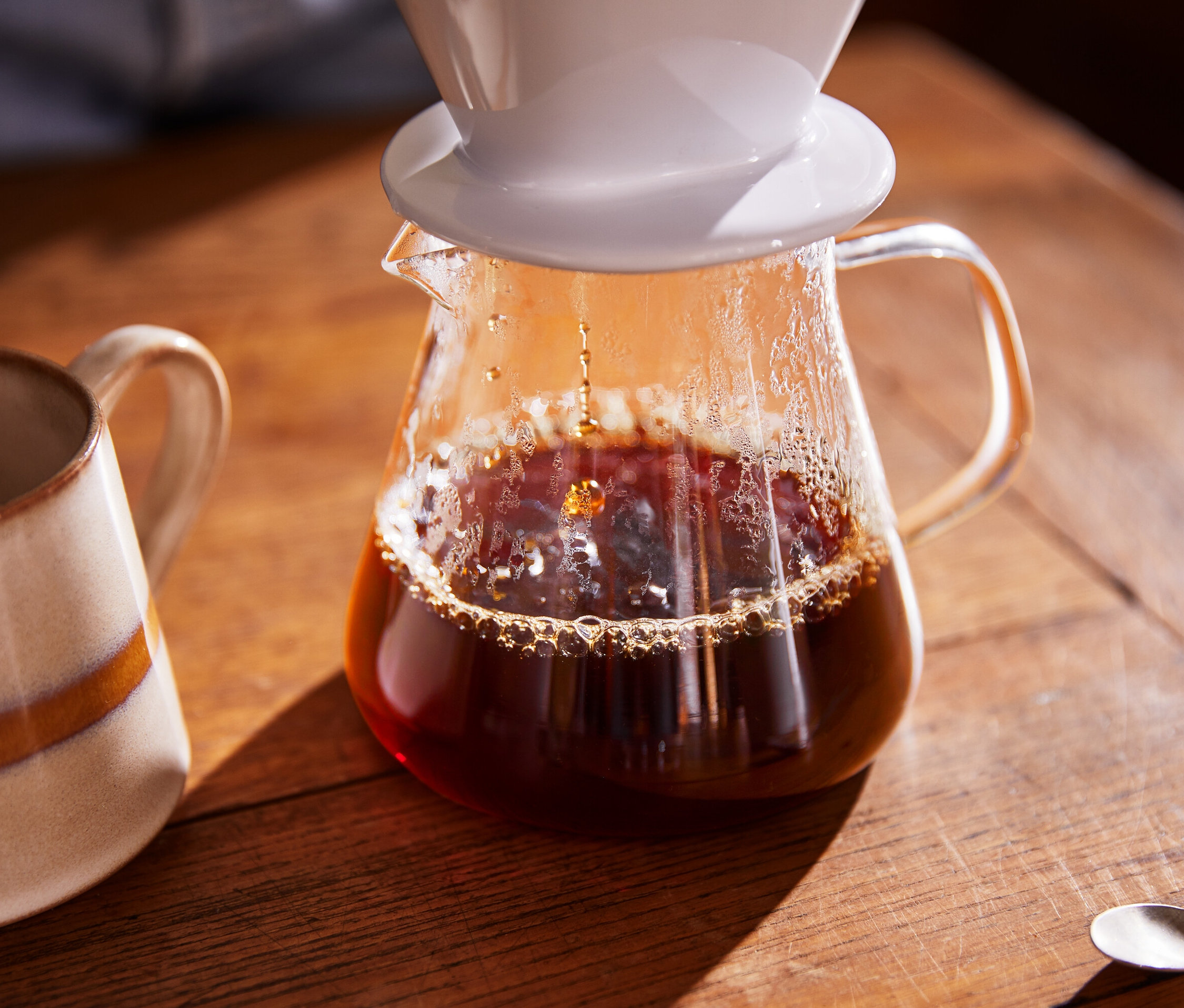 Kávé folyik egy üveg kávéskannába, mellette egy bögre.