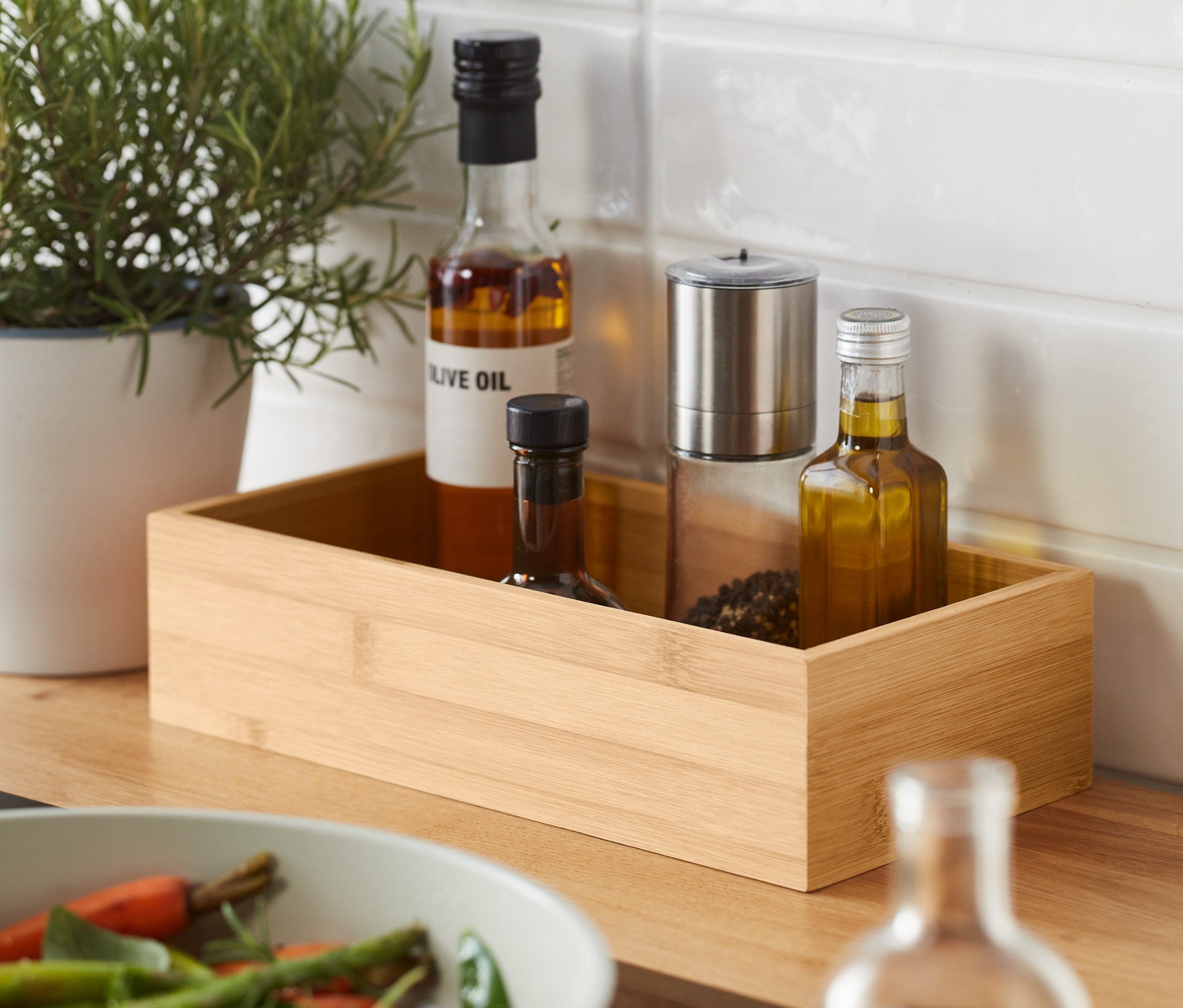 Fűszernövények egy cserépben és két bambusz fűszertartó egy serpenyő mellett, melyben zöldségek vannak.