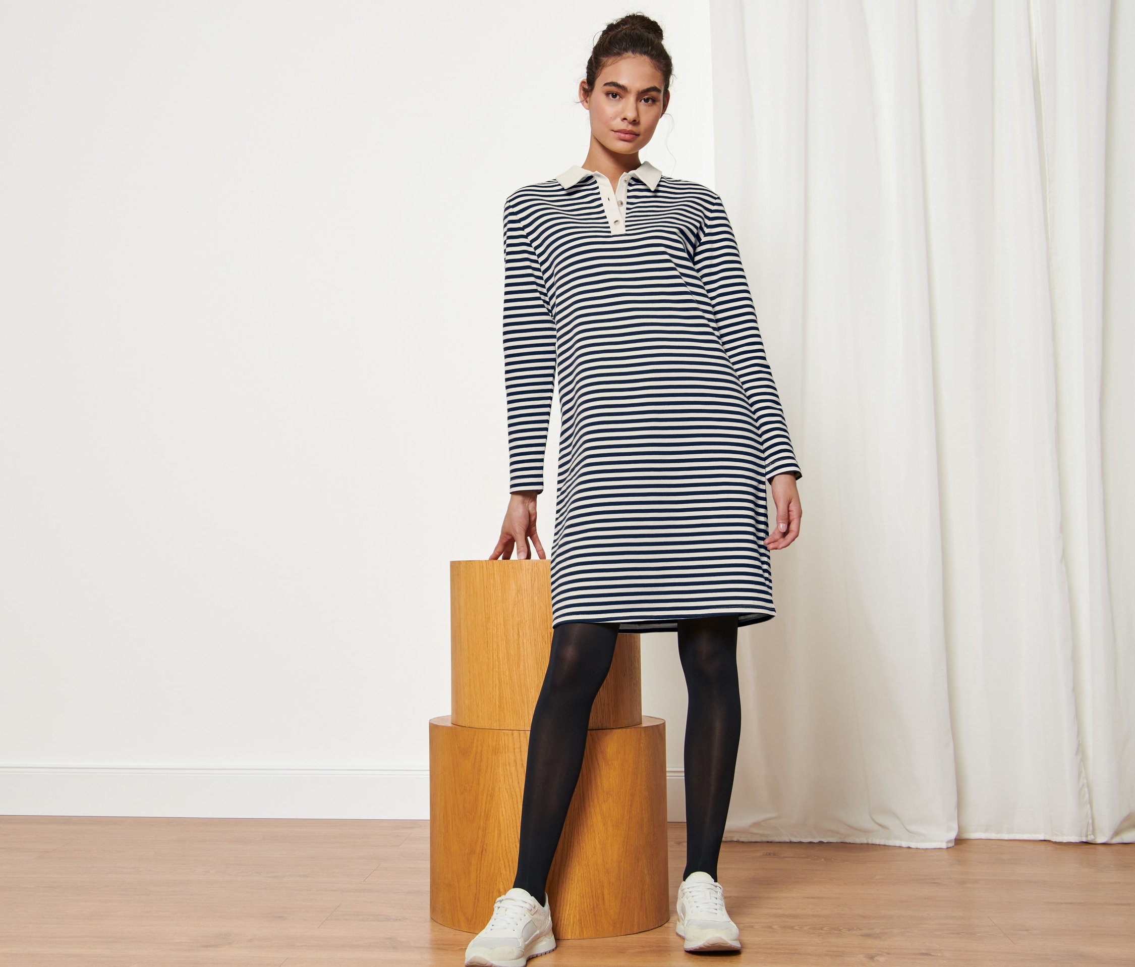 Nő pózol egy csíkos, krém/sötétkék színű női lezser ruhában.