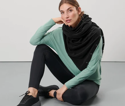 Nő ül a földön, fekete 3 az 1-ben oversize sálat visel.
