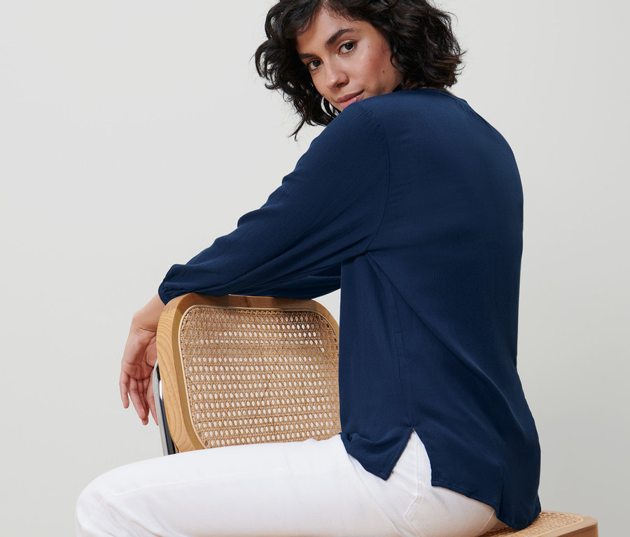 Nő ül oldalt egy széken, kék tunikablúzt visel.