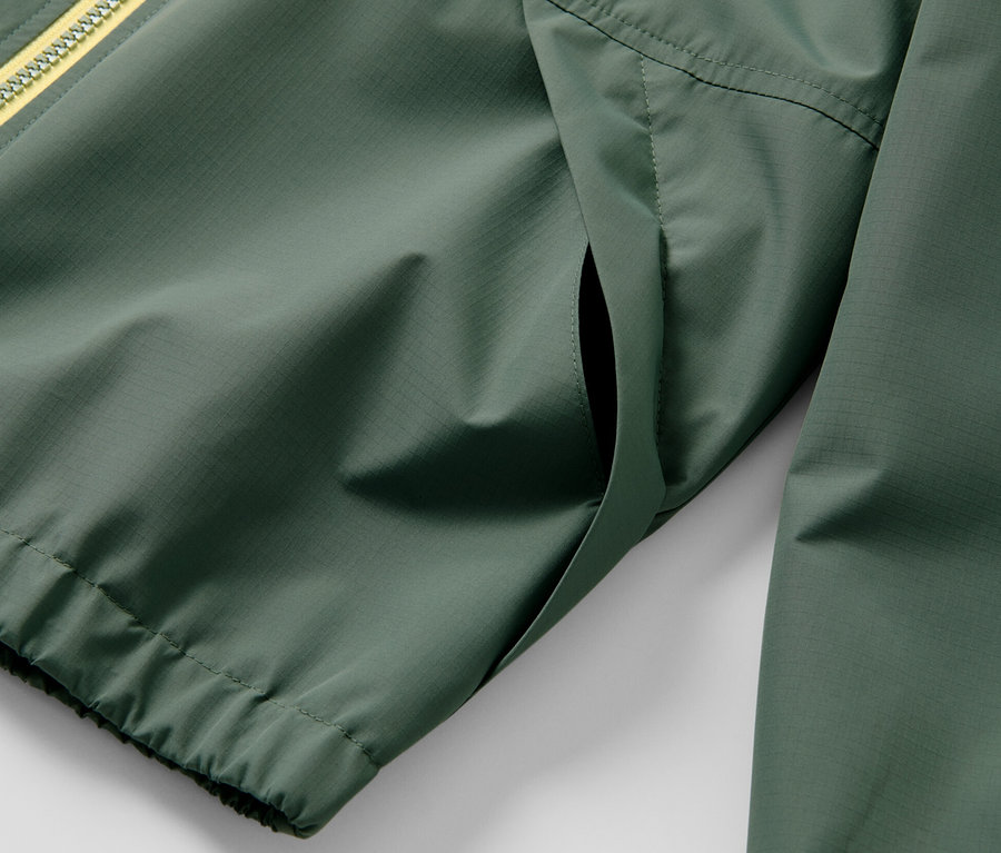 Egy zöld gyerek sportdzseki részletének képe sárga cipzárral.