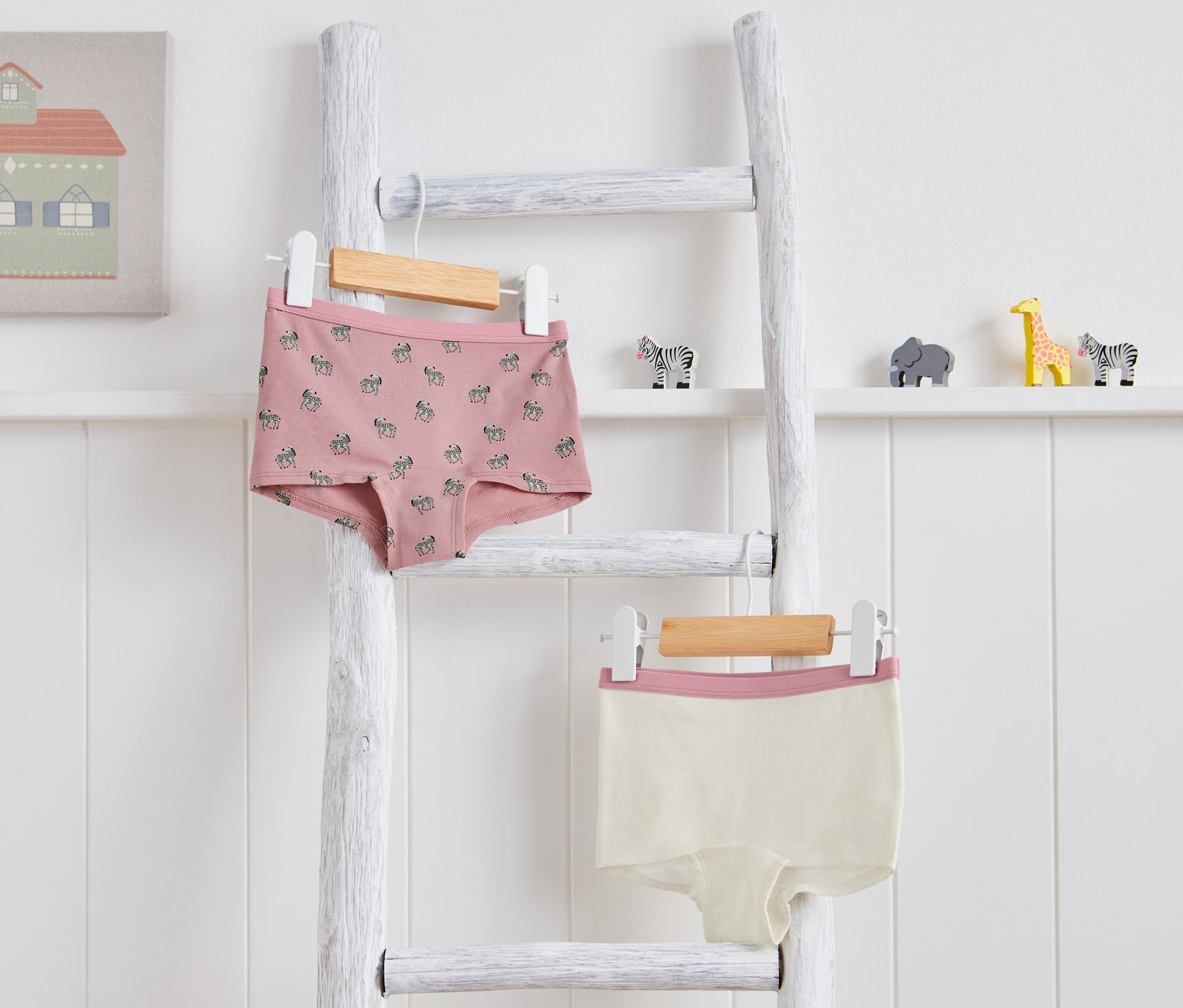 Két kislány magasderekú alsó, zebrás mintával, egy fehér létrán lóg. Az egyik rózsaszín zebrás mintával, a másik krémszínű rózsaszín szegéllyel.