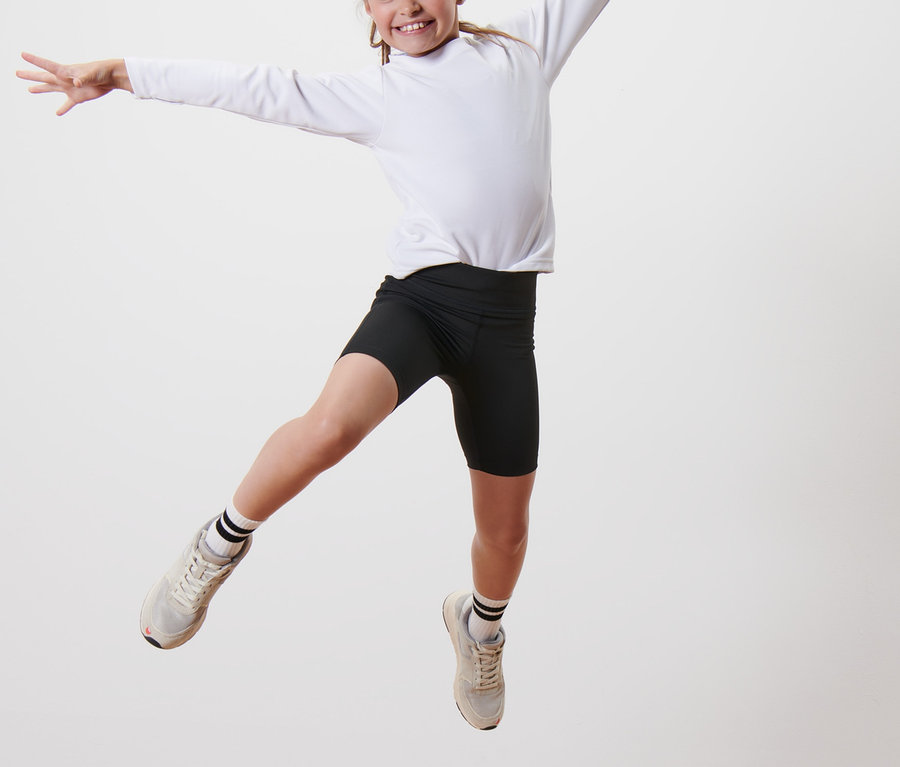 Egy lány ugrál egy faemelvényen, fekete sportnadrágot és fehér, hosszú ujjú inget visel. Rajta van a 2 gyerek sportrövidnadrág.