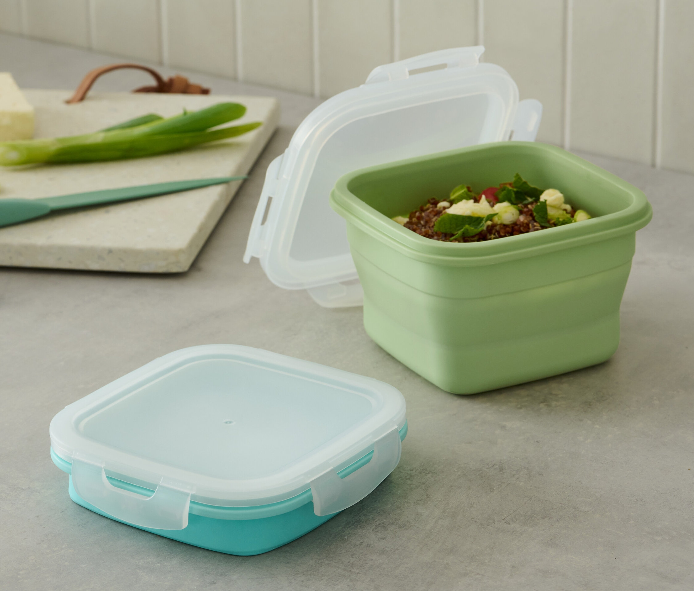 Két frissentartó doboz az asztalon. Egyikük zöld és nyitott, a másikuk türkiz és zárt.