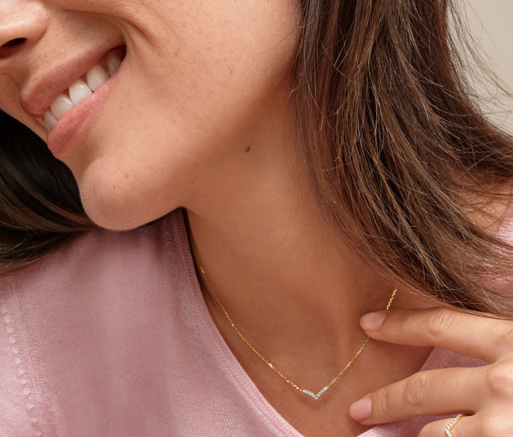 Nő arany nyaklánccal, V alakú medállal, cirkóniával és V alakú arany gyűrűvel, cirkóniával.