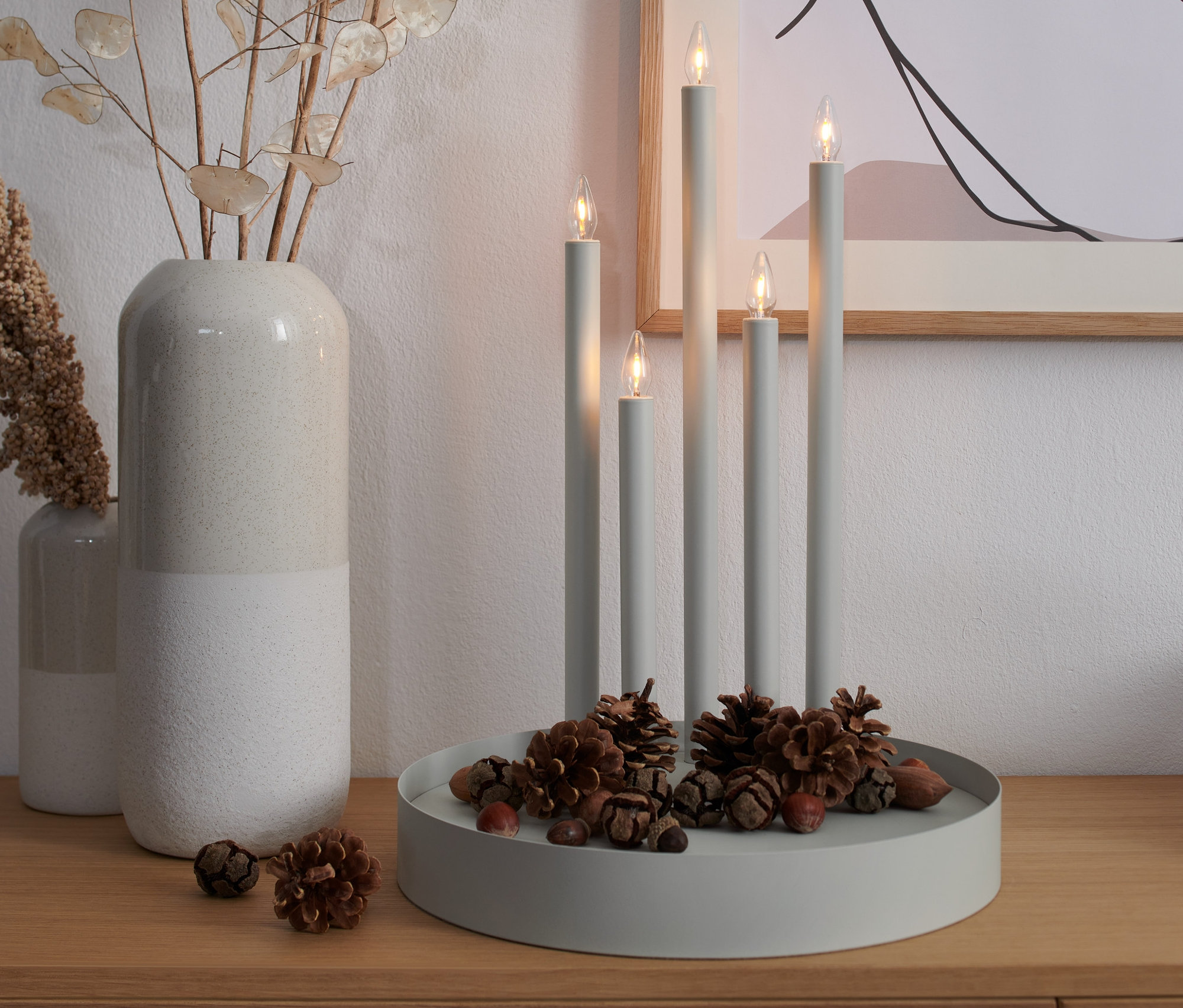 Szürke LED-es gyertyatartó öt gyertyával és tobozokkal egy fa asztalon.