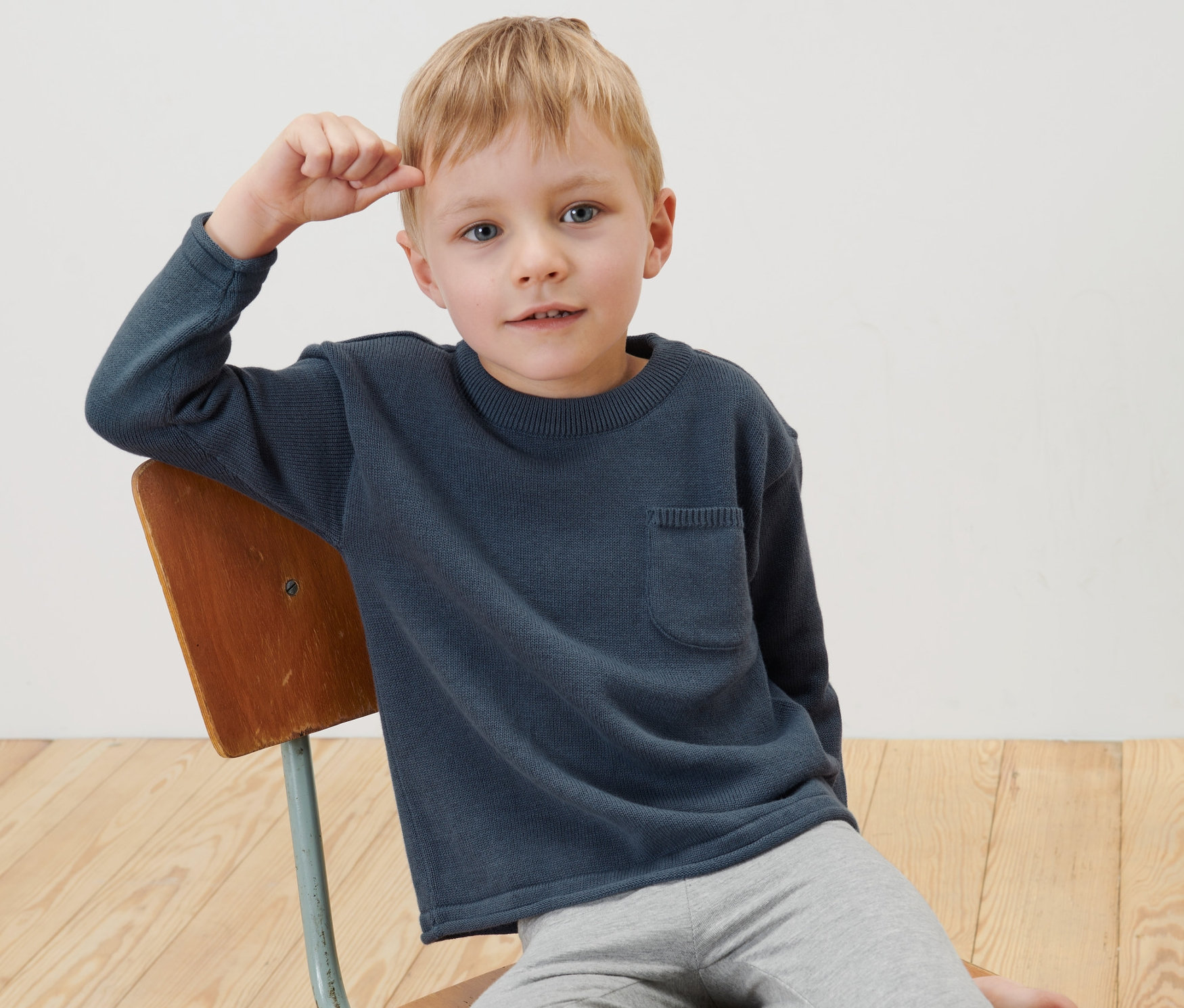 Egy kisfiú ül egy széken és sötétkék gyerek kötött pulóvert visel.