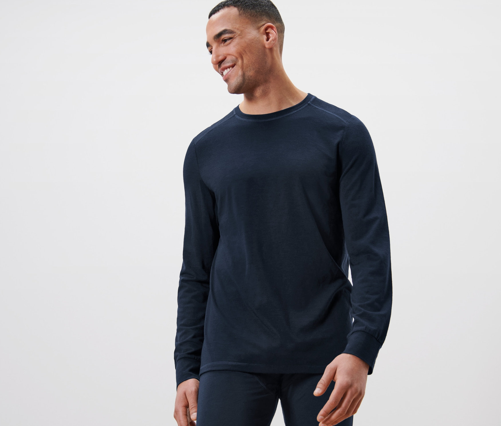 Mosolygó férfi sötétkék, RWS minősítésű gyapjú hosszú ujjú felsőt visel.