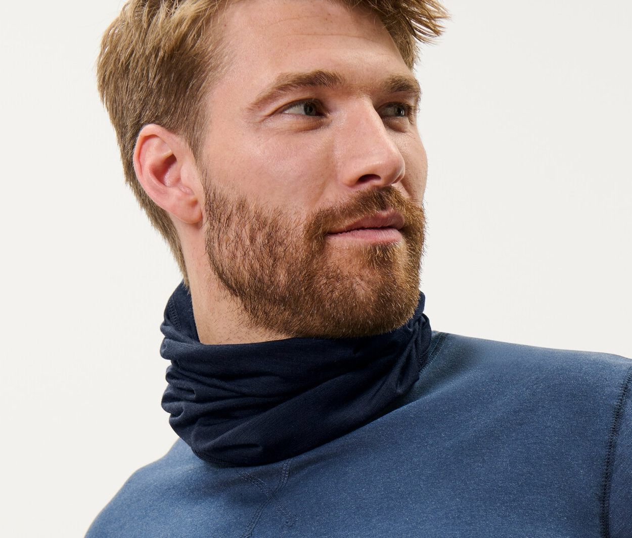 Barna hajú férfi kék, RWS minősített gyapjú multifunkcionális kendőt és kék felsőt visel.