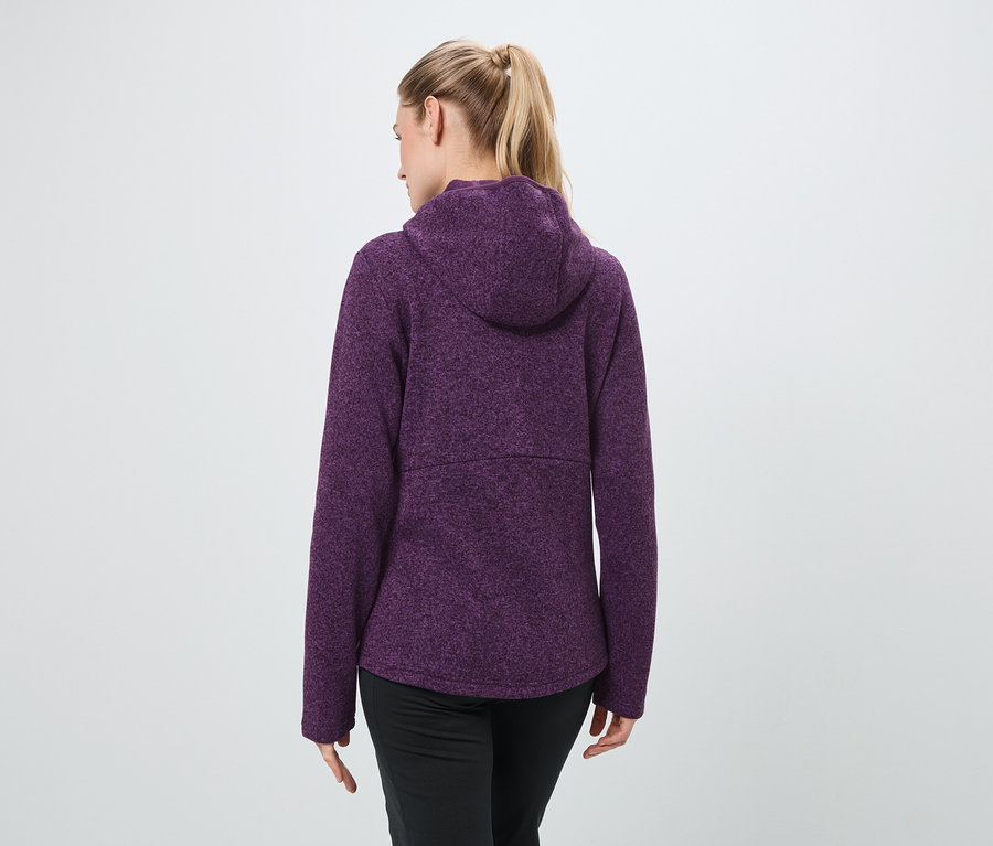 Hátulról látható egy szőke hajú, lófarokba kötött nő, aki lila kapucnis pulóvert és fekete nadrágot visel.