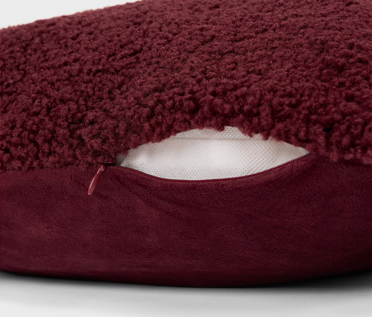 Egy bordó, bozontos párna részlete cipzárral.